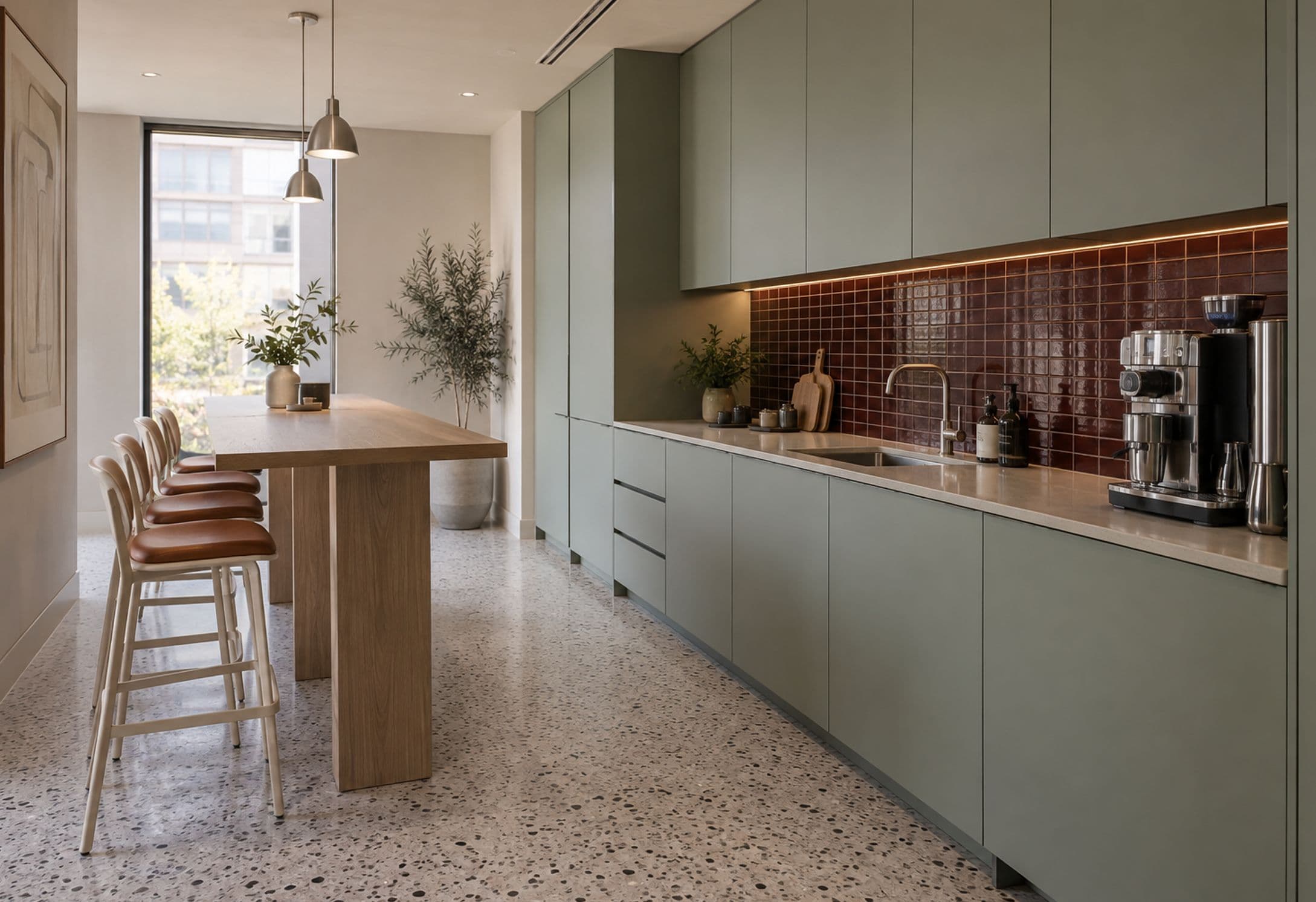 Sage green kitchen run with a glazed oxblood tile splashback and an oak bar table with leather stools